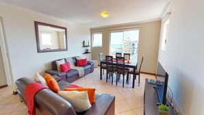 A living room with a sofa, dining table, chairs, and a TV. - Mont Blu Condo (Cape Town)