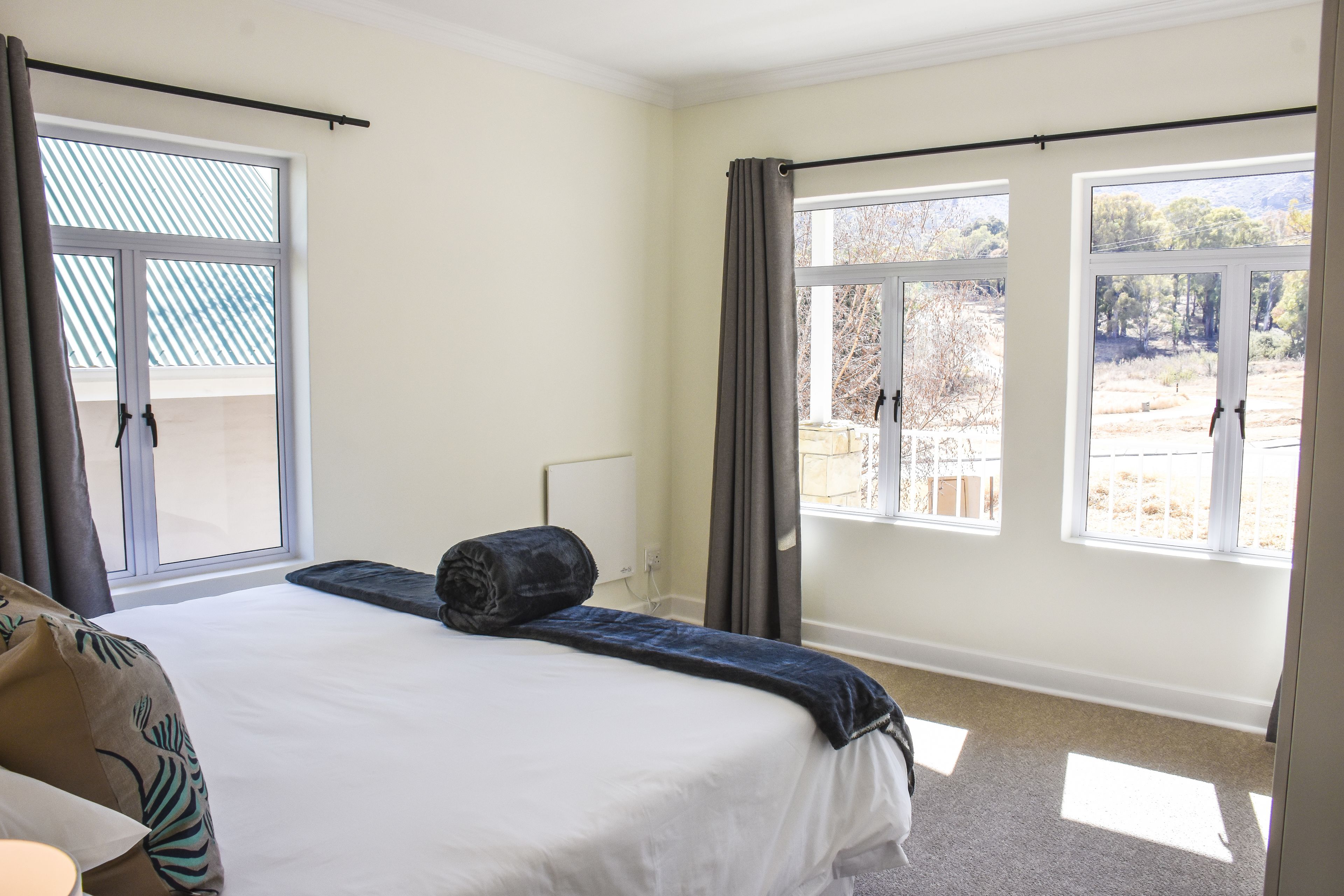A bedroom with a large bed, two windows, and a view of the outdoors.