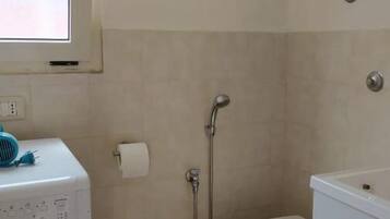A compact bathroom with a washing machine, toilet, and shower.