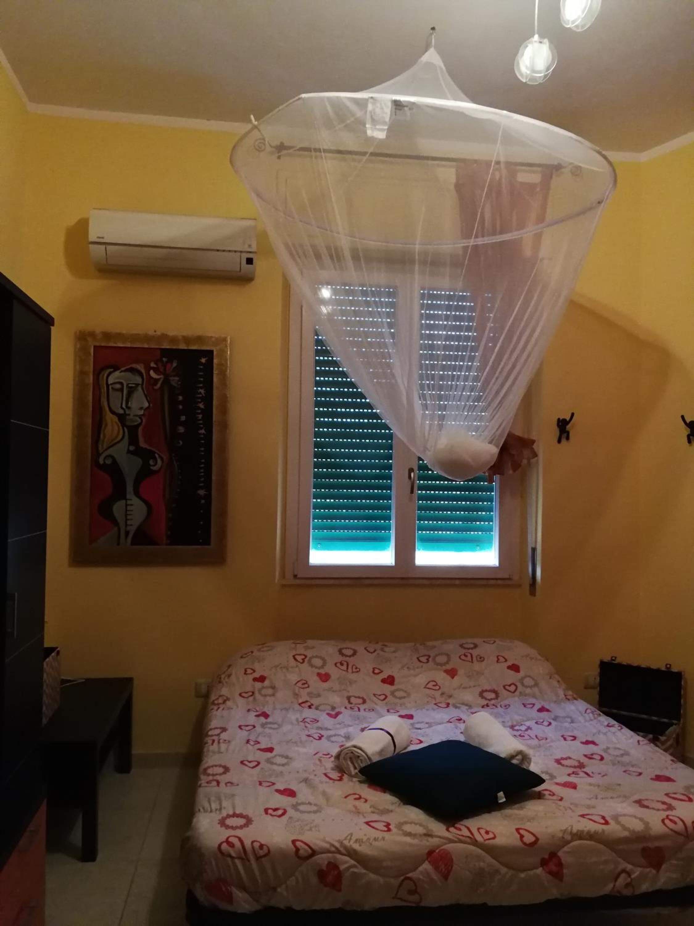 Une chambre à coucher avec un lit, une moustiquaire, une fenêtre avec des stores et un climatiseur fixé au mur.