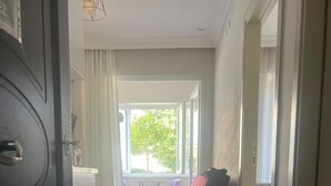 A hallway with a patterned rug, a dark sofa with a red cushion, and a window with a view of greenery outside. - Safrangold pansiyon (Karabük)