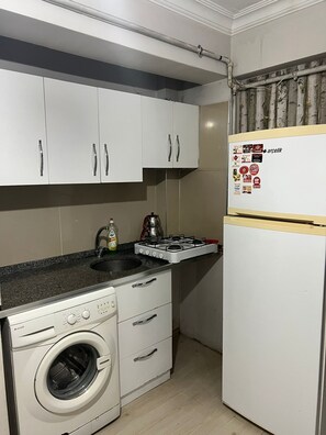Una cocina compacta con muebles blancos, lavadora integrada, cocina a gas y refrigerador con calcomanías.