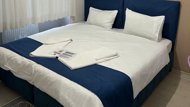 A neatly made bed with a blue headboard, white bedding, and a folded towel on the bed. - Safrangold pansiyon (Karabük)