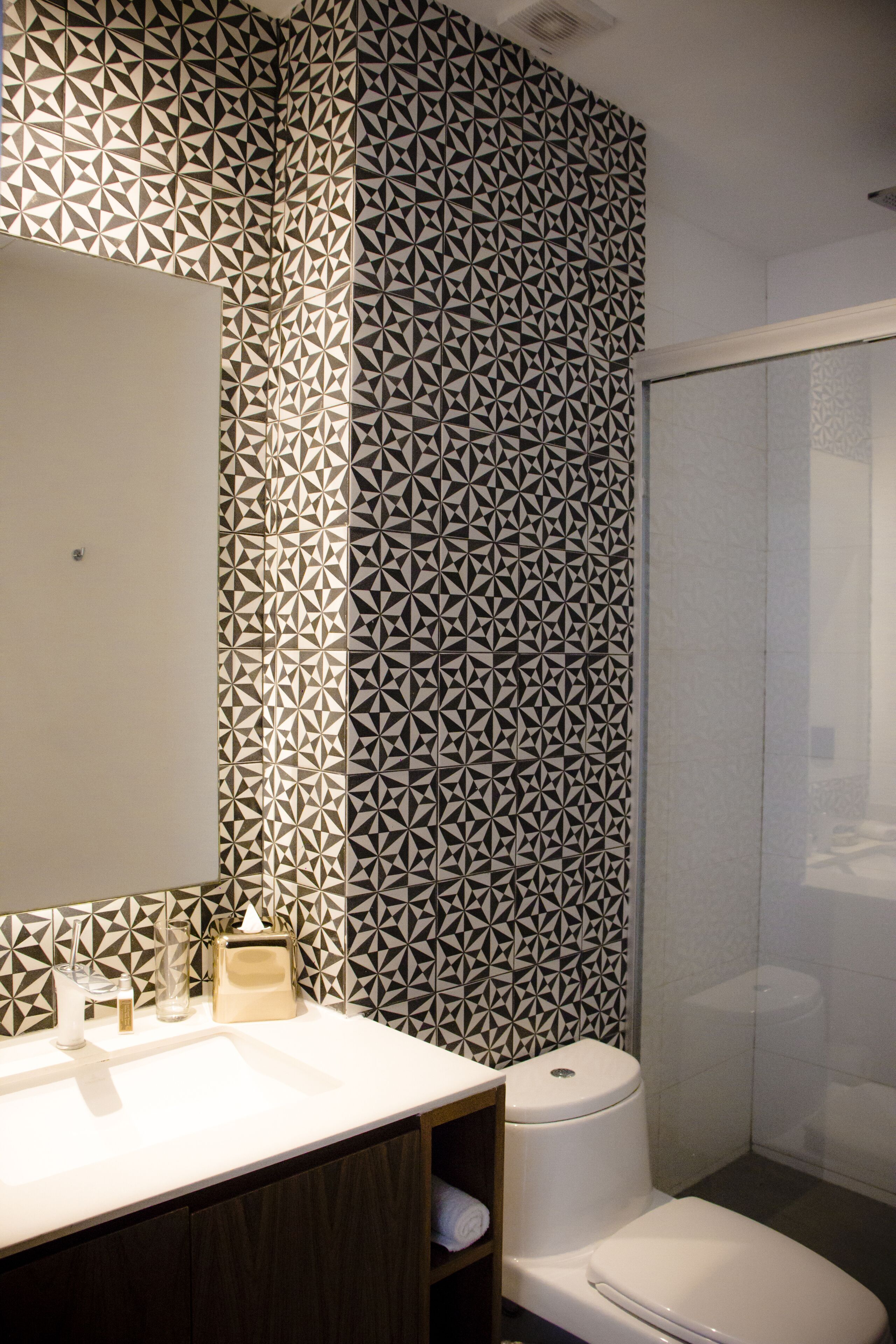 Un baño con pared de diseño geométrico, un lavamanos blanco y un inodoro.
