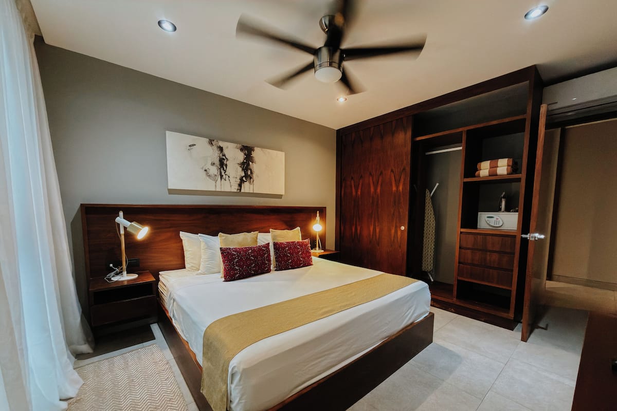 Un dormitorio moderno con una cama grande, cabecera de madera, lámparas de noche, ventilador de techo y un armario.