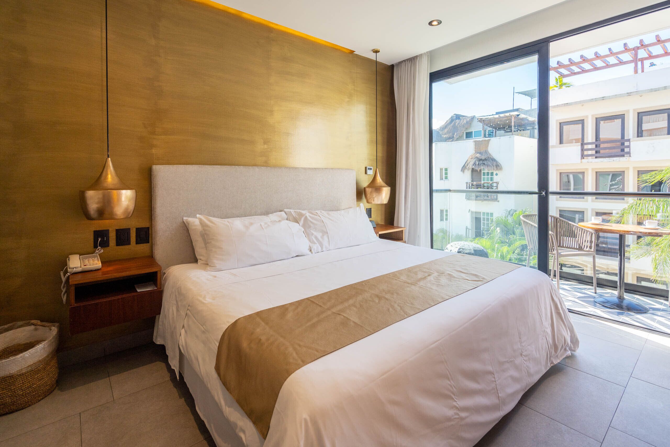 Habitación de hotel con una cama grande, mesitas de noche, un teléfono y vistas al balcón exterior.