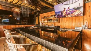 Eine Bar mit einer Marmorplatte, Korbstühlen und einer Holzwand mit Flaschenregalen.