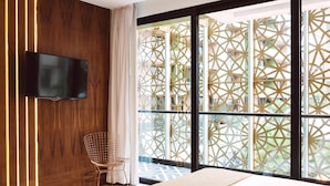 Ein modernes Hotelzimmer mit großem Fenster, einem Wand-Fernseher, einem Bett und einem Sessel.