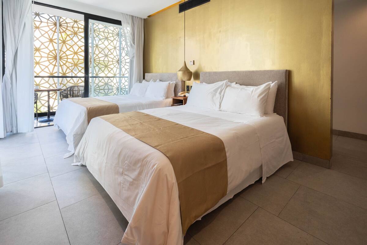 Habitación de hotel con una cama grande, una cama más pequeña y una zona de estar con vistas a través de una ventana con diseño.