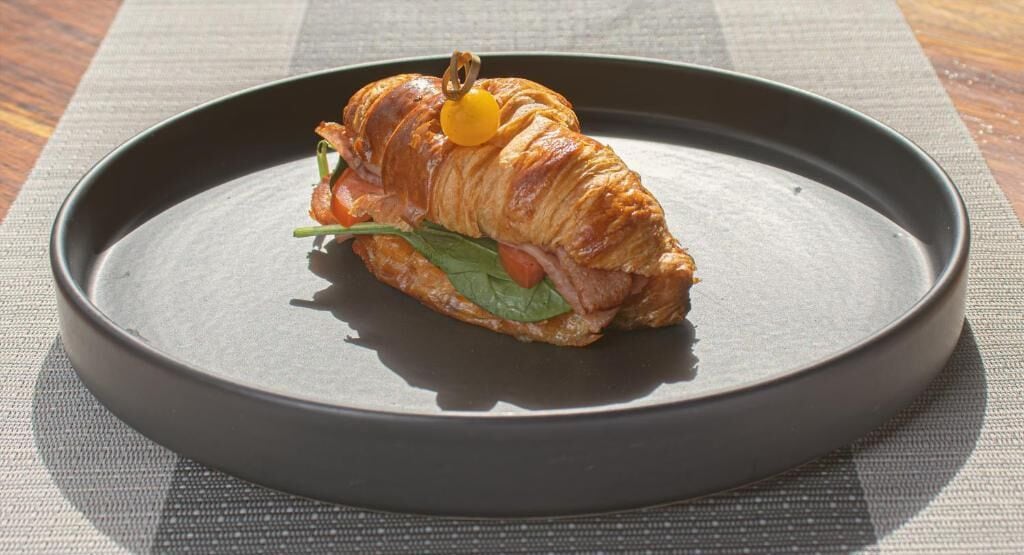 A croissant on a dark plate with a small yellow fruit on top, placed on a textured mat.