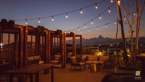 An outdoor patio area with string lights, wooden furniture, and a view of distant mountains. - IT Boutique Hotel & Restaurant (Playa del Carmen)