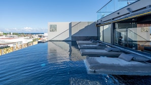 Ein Pool ohne Ende mit Liegestühlen und Blick auf die Stadt.