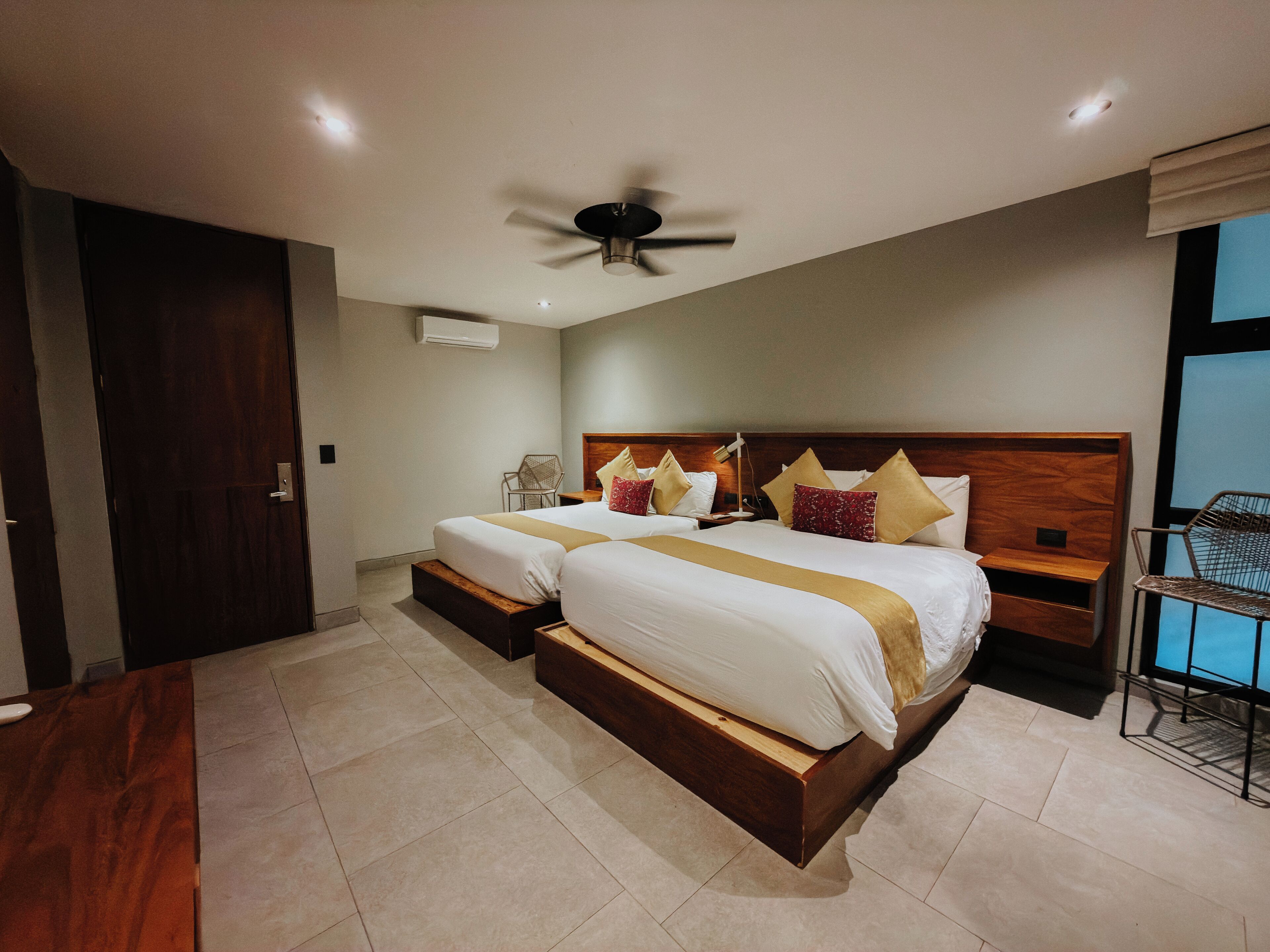 Une chambre d’hôtel avec deux lits, un ventilateur de plafond, une fenêtre et une chaise.