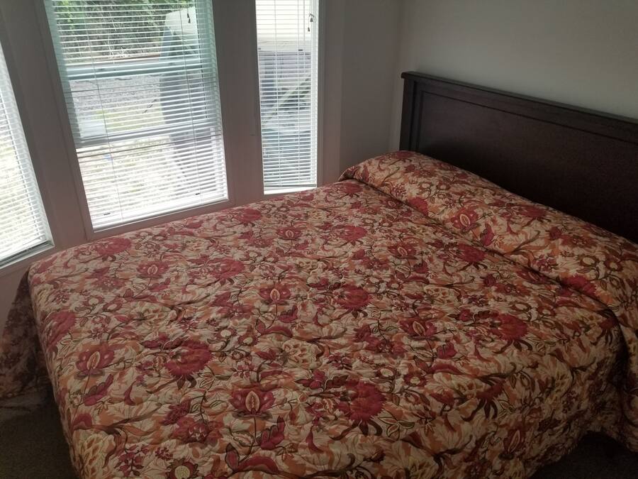 Un dormitorio con colcha estampada, cabecera de madera y ventana con persianas.