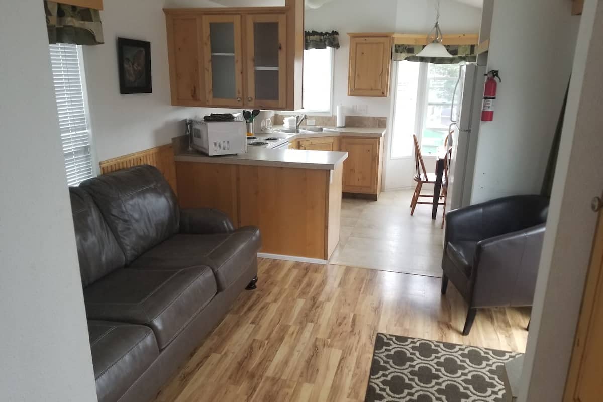 A modern kitchen with wooden cabinets, a built-in microwave, and a sink. There is a leather sofa and a chair in the living area.