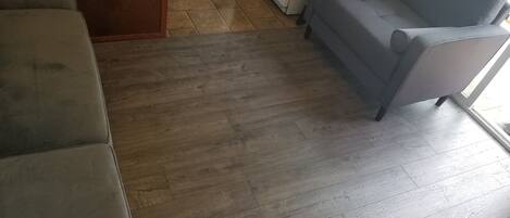 Una habitación con un sofá gris, suelo de madera y una puerta de madera.