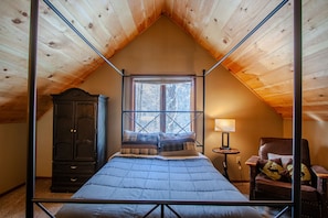 A bedroom with a sloped ceiling, a bed with a blue quilt, a wooden wardrobe, a chair with a cushion, and a small table with a lamp. - Private Cottage Nestled in the Trees;Pet Friendly-Near Slopes-Waterpks-JimThorpe (Albrightsville)
