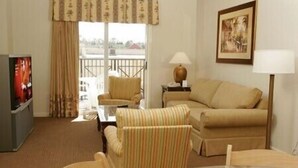 Una habitación de hotel con sofá, sillones, televisión, lámpara y un cuadro en la pared.