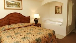 Una habitación de hotel con cama, una mesita de noche con lámpara, un cuadro en la pared y una bañera.