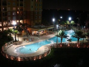 A nighttime view of a hotel pool area with a circular water feature, lounge chairs, and palm trees. - Luxury Condo,Pirate Ship,Near Disney,Renovated,FREE Wif & Parking,Kids club (orlando)