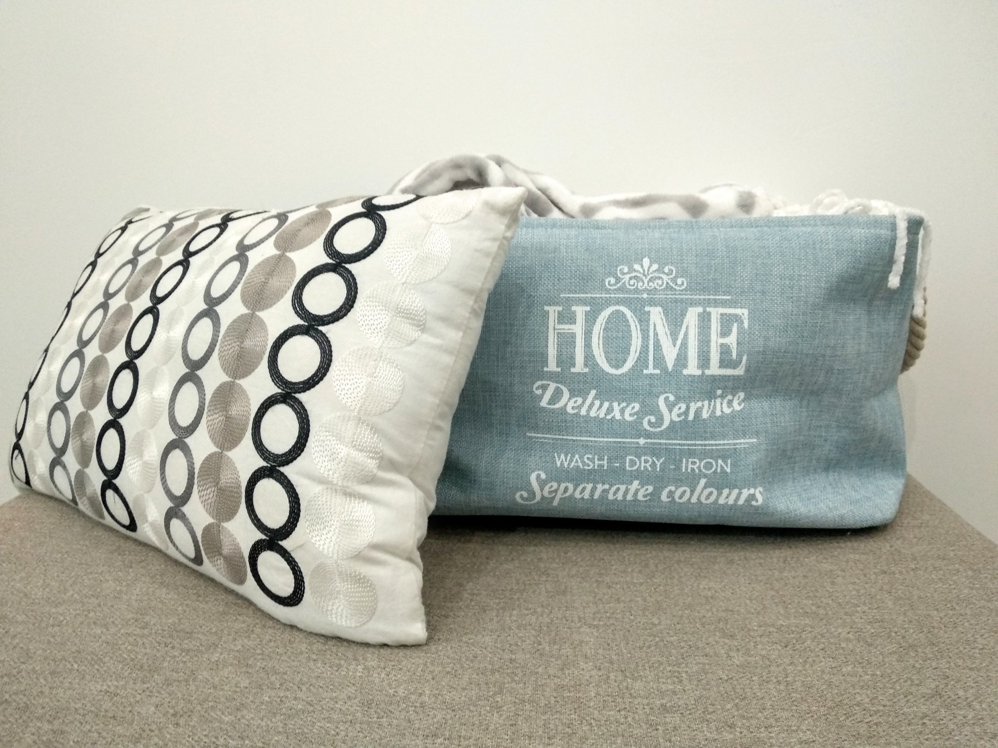 A grey and white pillow with a circular pattern and a blue pillow with embroidered text.