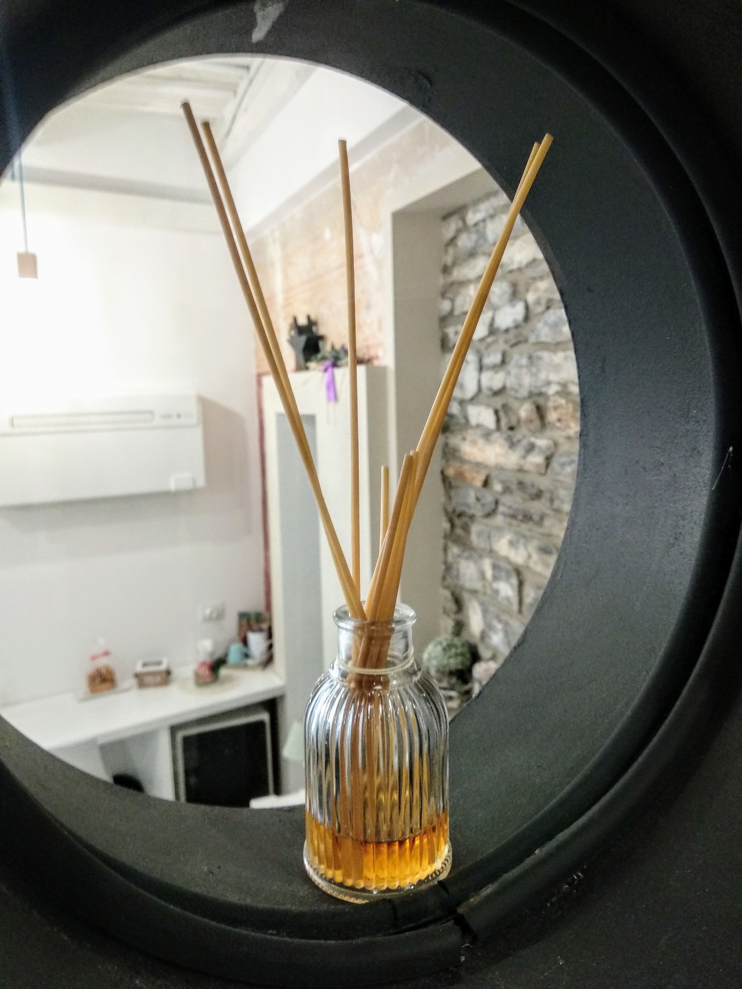 Un vaso di vetro con bastoncini di canna attraverso una finestra circolare.