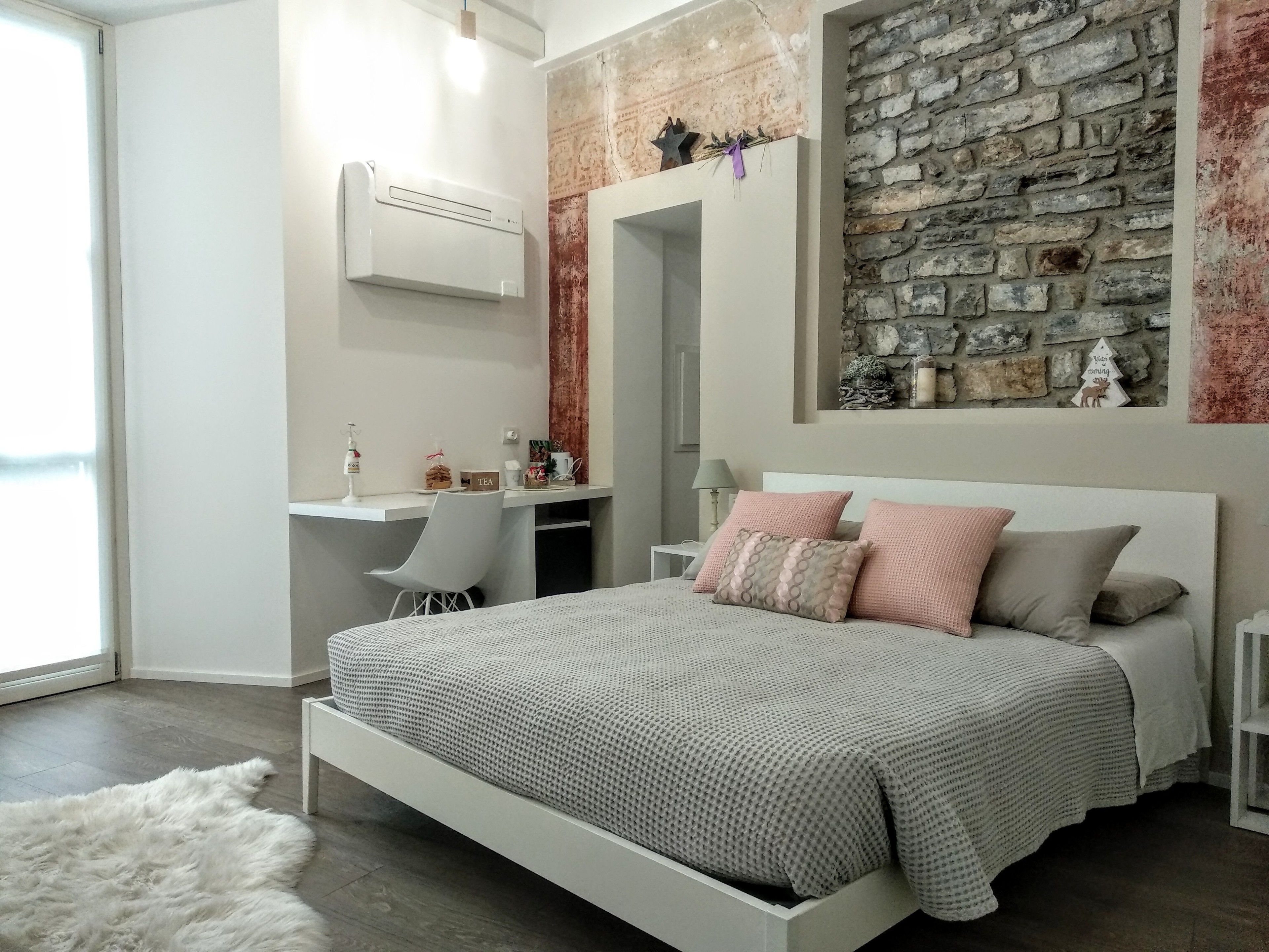 Une chambre moderne avec un mur d’accent en pierre, un lit blanc et un bureau avec une chaise.