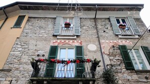 A building with stone walls, green shutters, and a balcony with red flowers.