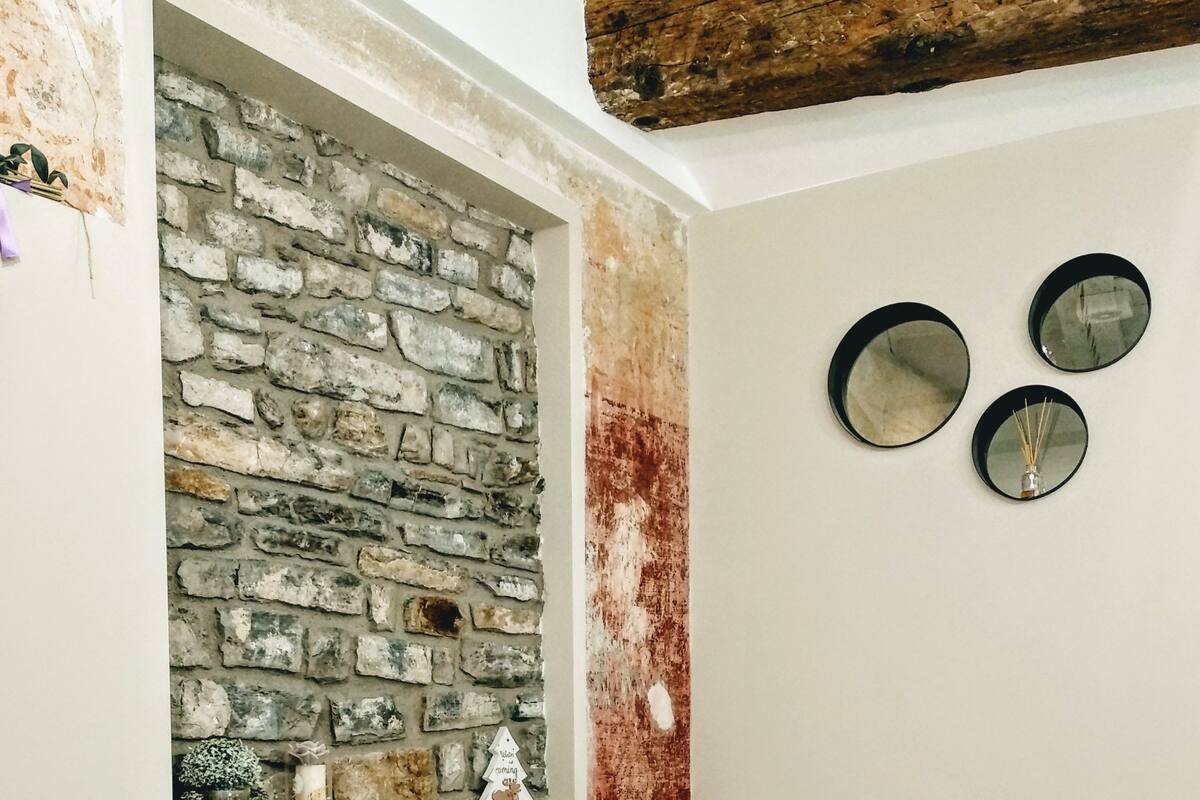 Un dormitorio con pared de piedra, una cama con ropa de cama blanca y rosa, y dos mesitas de noche con lámparas.