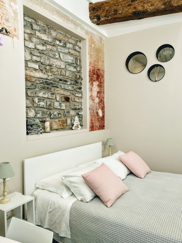 A bedroom with a stone wall, a bed with white and pink bedding, and two bedside tables with lamps.