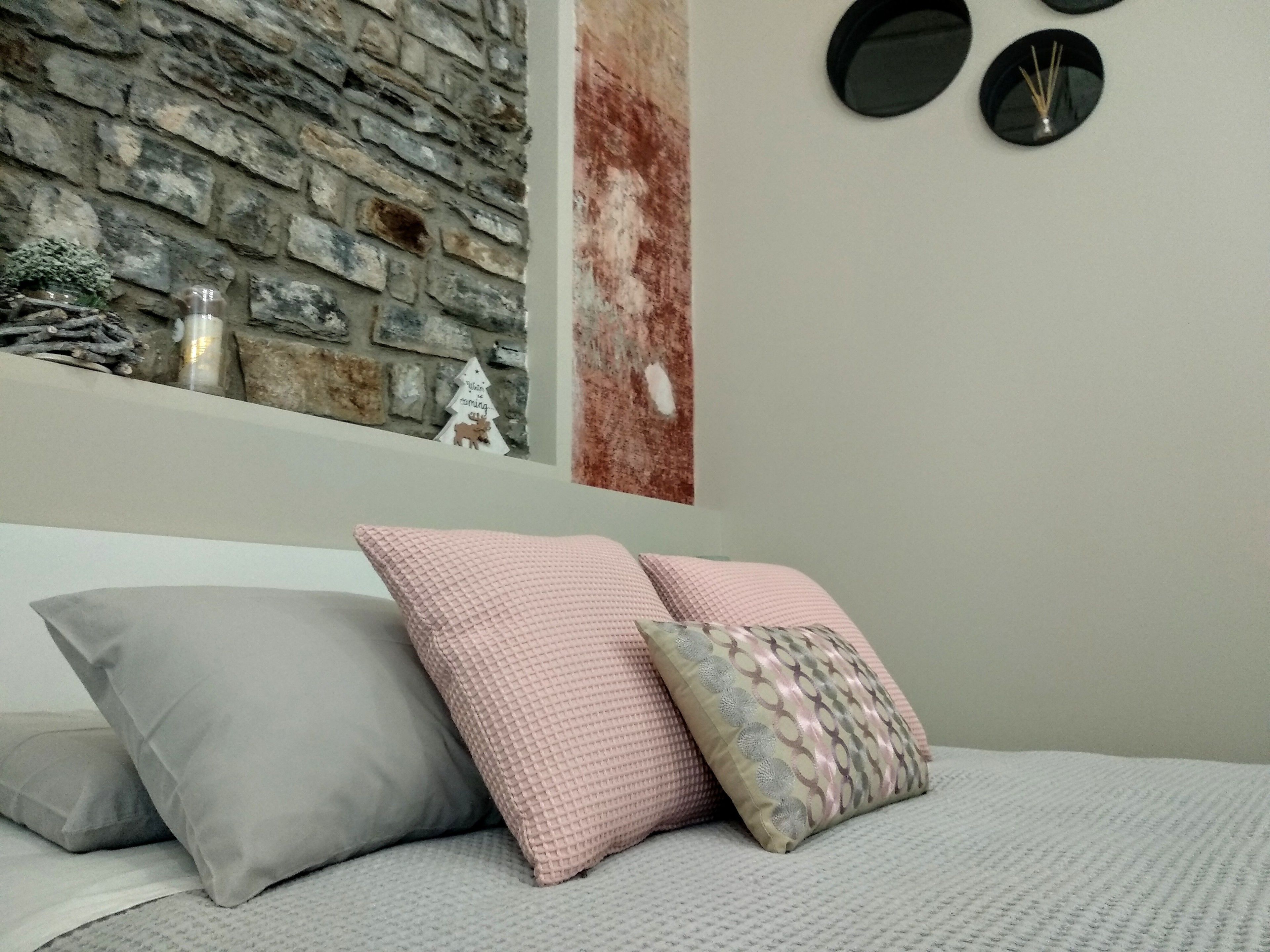 A bedroom with a stone wall, a bed with grey and pink pillows, and a wall-mounted clock.