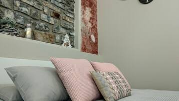 A bedroom with a stone wall, a bed with grey and pink pillows, and a wall-mounted clock.