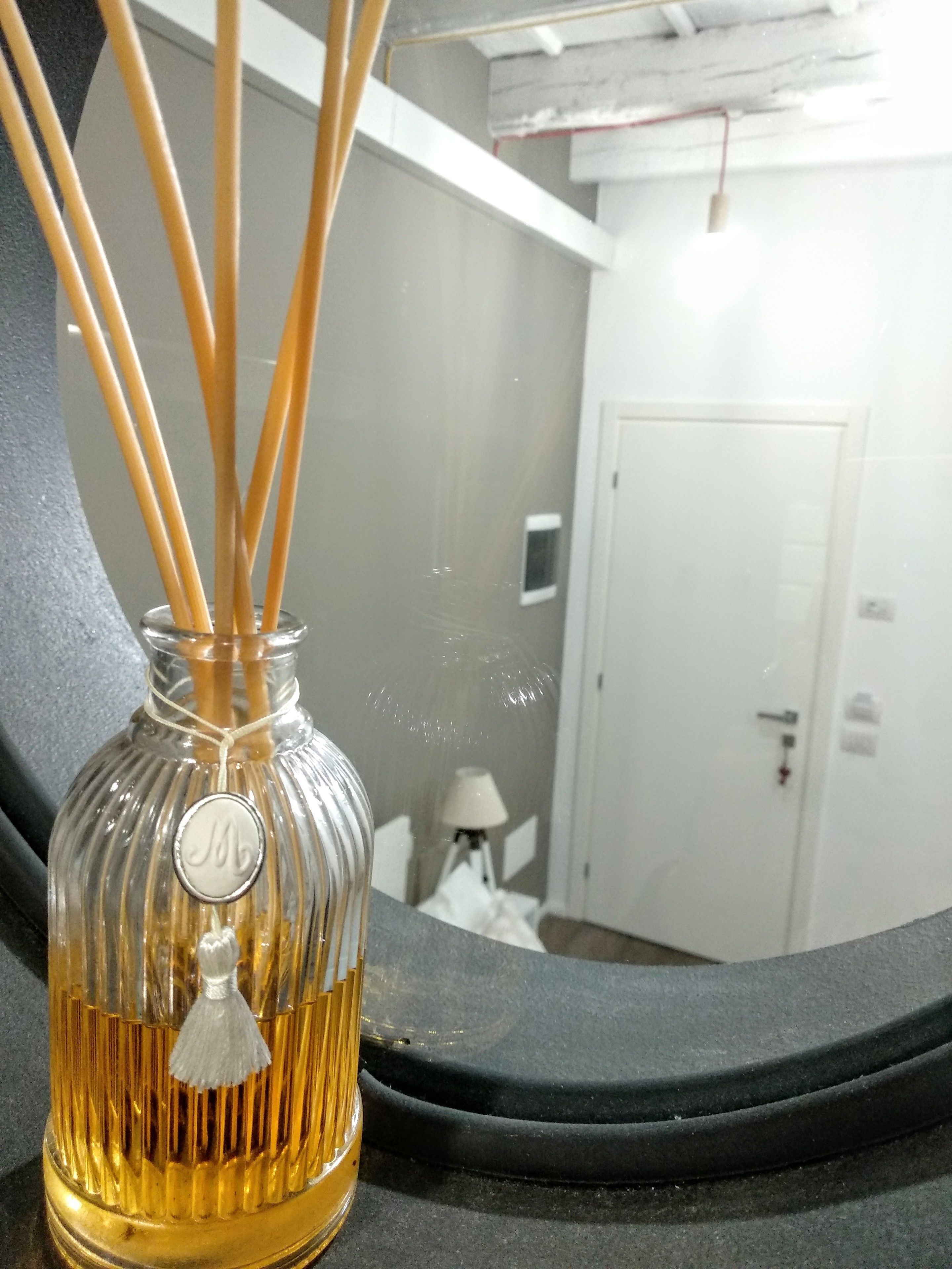Une bouteille en verre ornée d’un emblème métallique, une porte blanche et une lampe en arrière-plan.