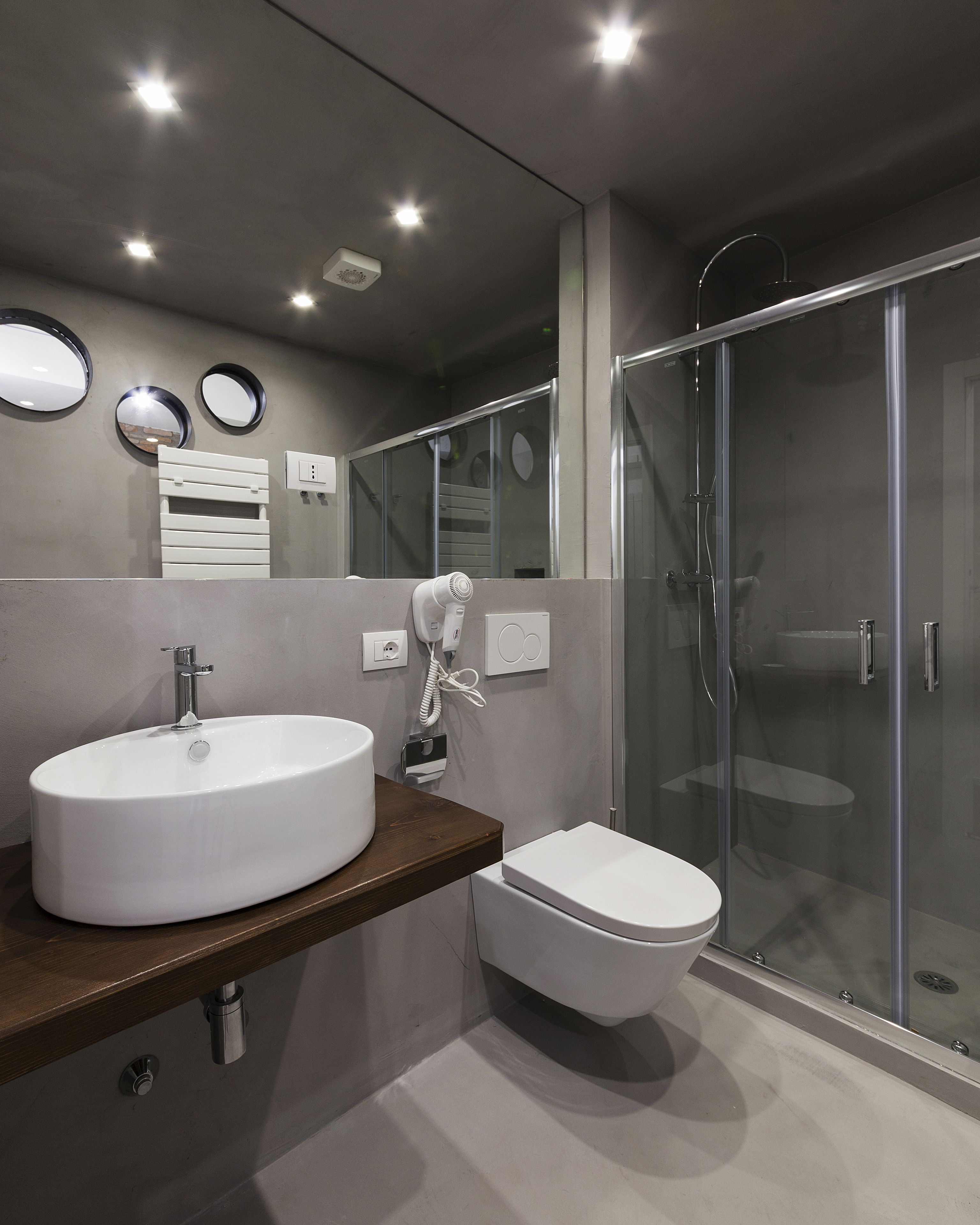 Un baño moderno con un lavamanos grande blanco, un inodoro y una ducha con mampara de vidrio.