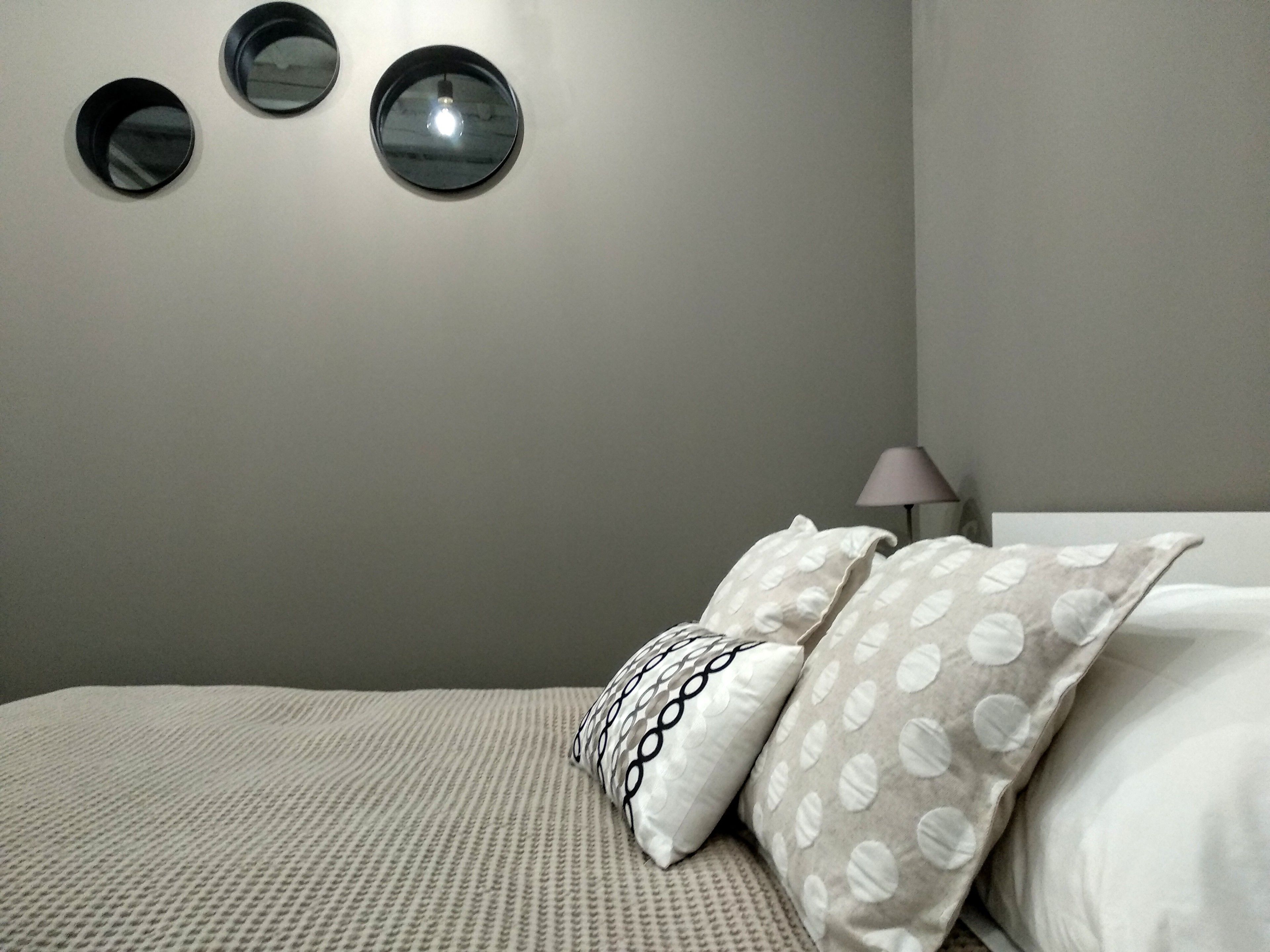 Un dormitorio con cama, almohadas, una lámpara y tres espejos fijados a la pared.