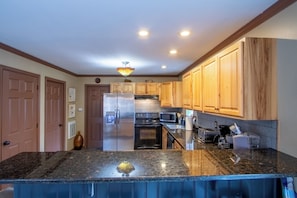 A kitchen with wooden cabinets, a refrigerator, a stove, a microwave, and a granite countertop.