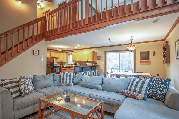 A spacious living room with a large sectional sofa, a wooden coffee table, and a staircase leading to an upper level.
