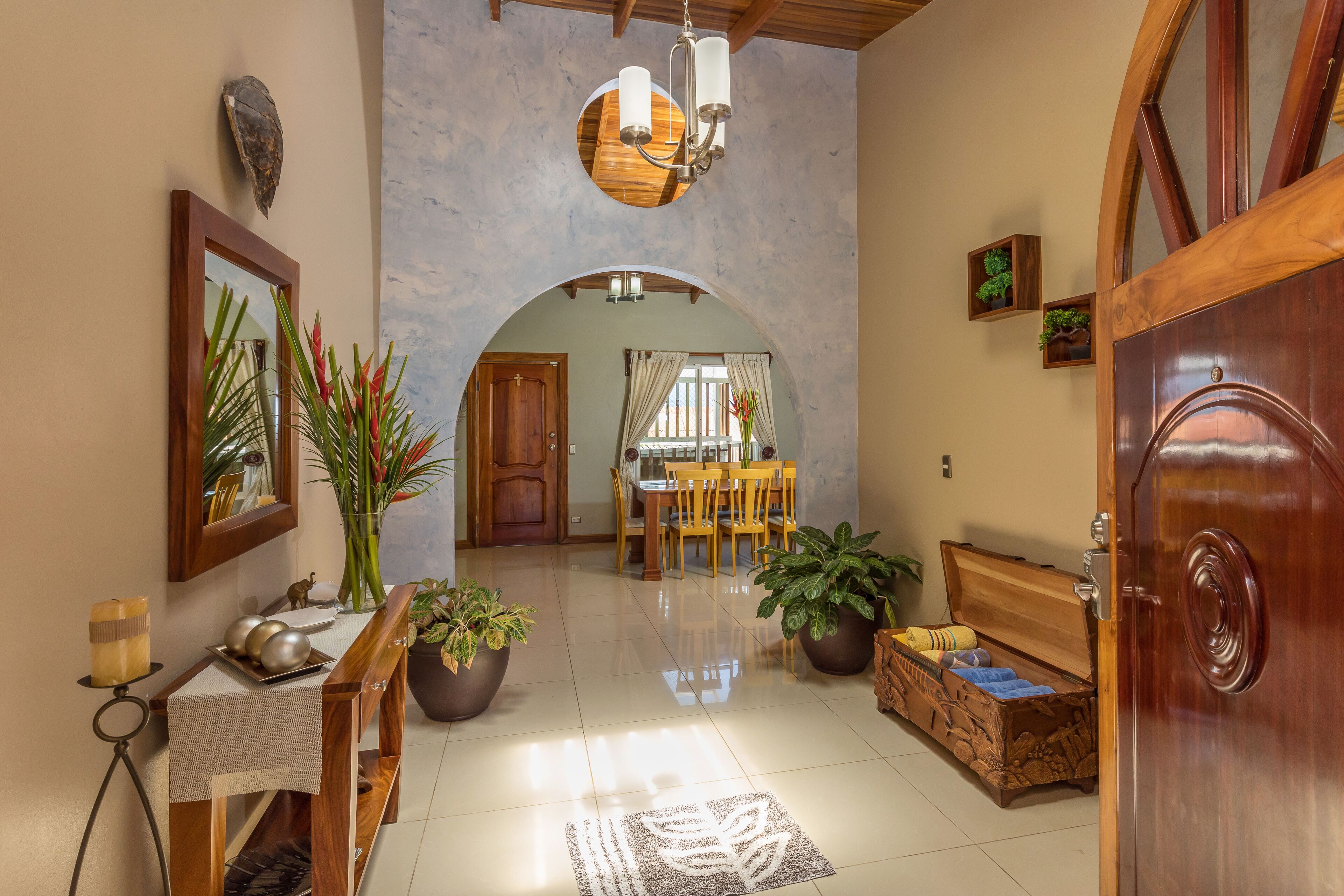 Uma sala ampla com um banco de madeira, uma mesa de jantar com cadeiras, um armário de madeira e um espelho grande.