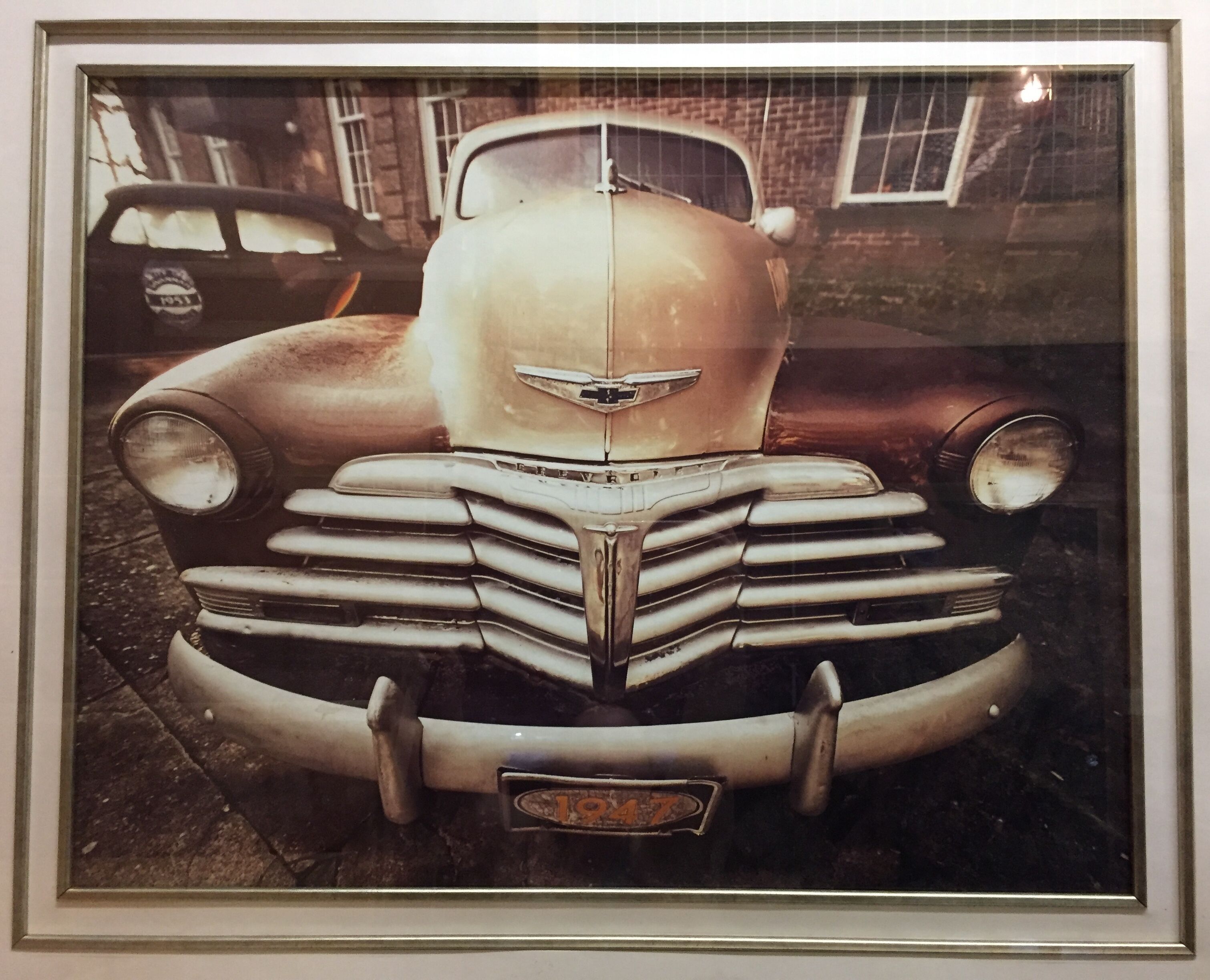 Un coche antiguo con una prominente rejilla frontal y emblema, estacionado frente a un edificio con ventanas y fachada de ladrillo.