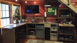 A cozy kitchen with a wooden interior, a TV mounted on the wall, a Christmas tree, and a 'Full Serve' sign.