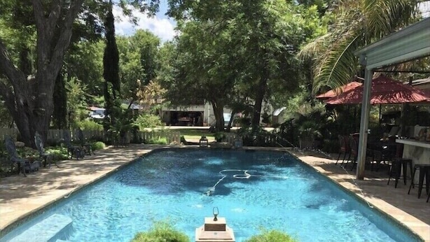 A rectangular swimming pool with a stone deck, surrounded by trees and a covered seating area.