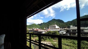 A view from a window with a wooden frame, overlooking a river, buildings, and a mountain.