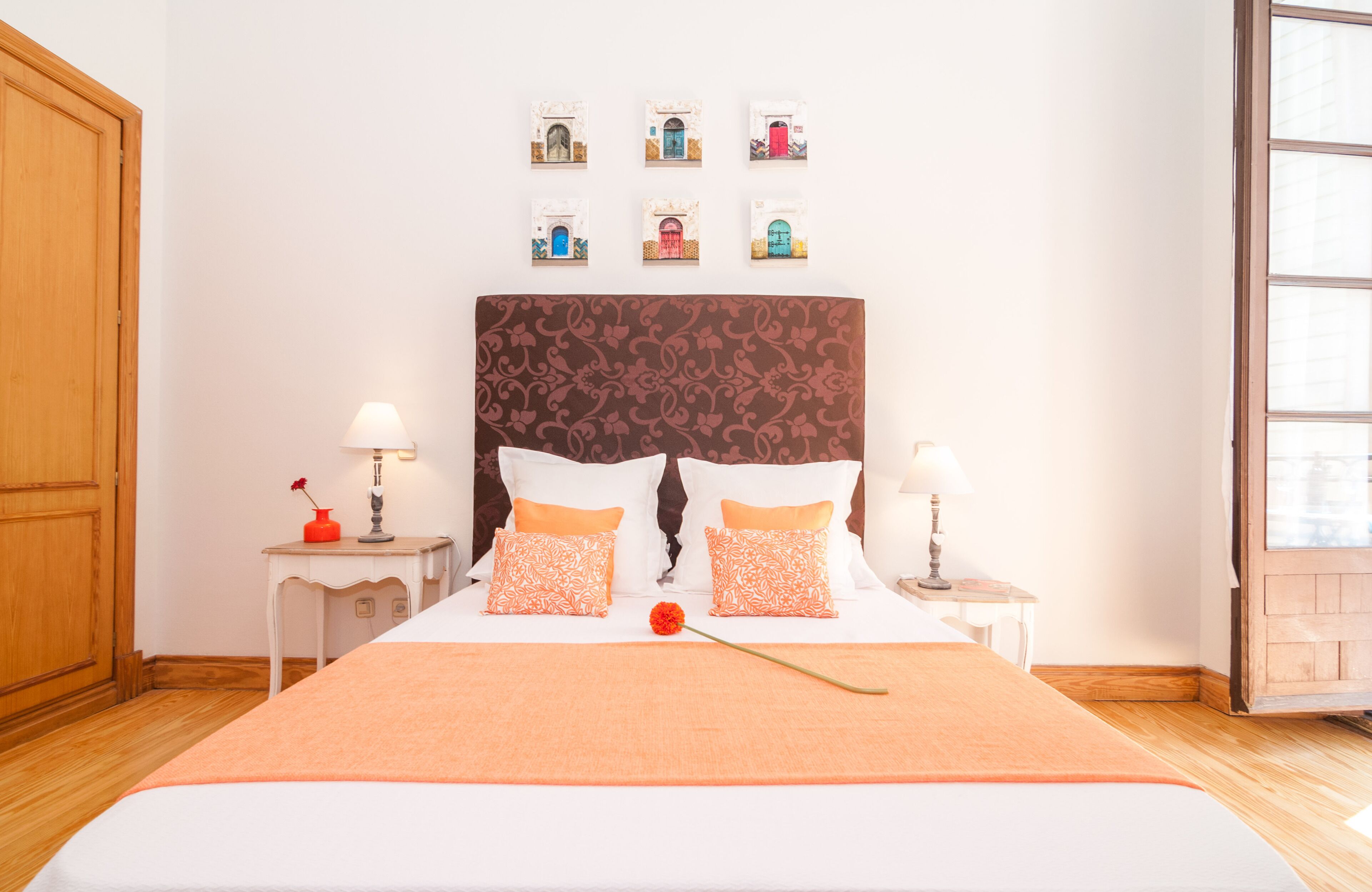 Un lit bien fait, avec une tête de lit à motifs, deux tables de chevet avec des lampes et un mur orné de tableaux encadrés.
