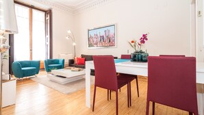 A modern living room with teal armchairs, a red sofa, a white dining table, and a cityscape painting on the wall. - MADRID-SOL-GATE PLAZA MAYOR, New Apartment, Comodo, modern design. (Madrid)