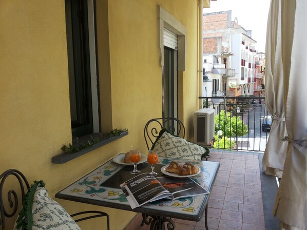 A balcony with a table set for breakfast, including croissants and orange juice, and a book titled "McLuhan & McLuhan".