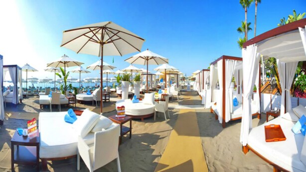 Ein Strandresort mit mehreren weißen Cabanas, Sonnenschirmen und Liegestühlen.