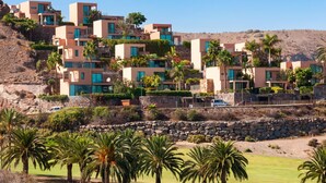 A coastal residential area with modern buildings, palm trees, and a clear sky.