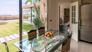 A modern kitchen with a glass dining table, a refrigerator, and a view of a landscaped outdoor area.