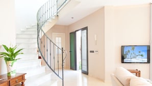 A modern living room with a spiral staircase, a flat-screen TV mounted on the wall, and a potted plant on a wooden table.