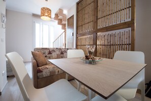 Un espace repas moderne avec une table en bois, des chaises blanches et un canapé à motifs.